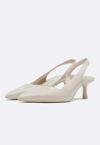 Bež slingback pete z ostrim prstom, teksturiranim materialom, 5 cm zoženim petom in izrezi na straneh za eleganten dizajn.