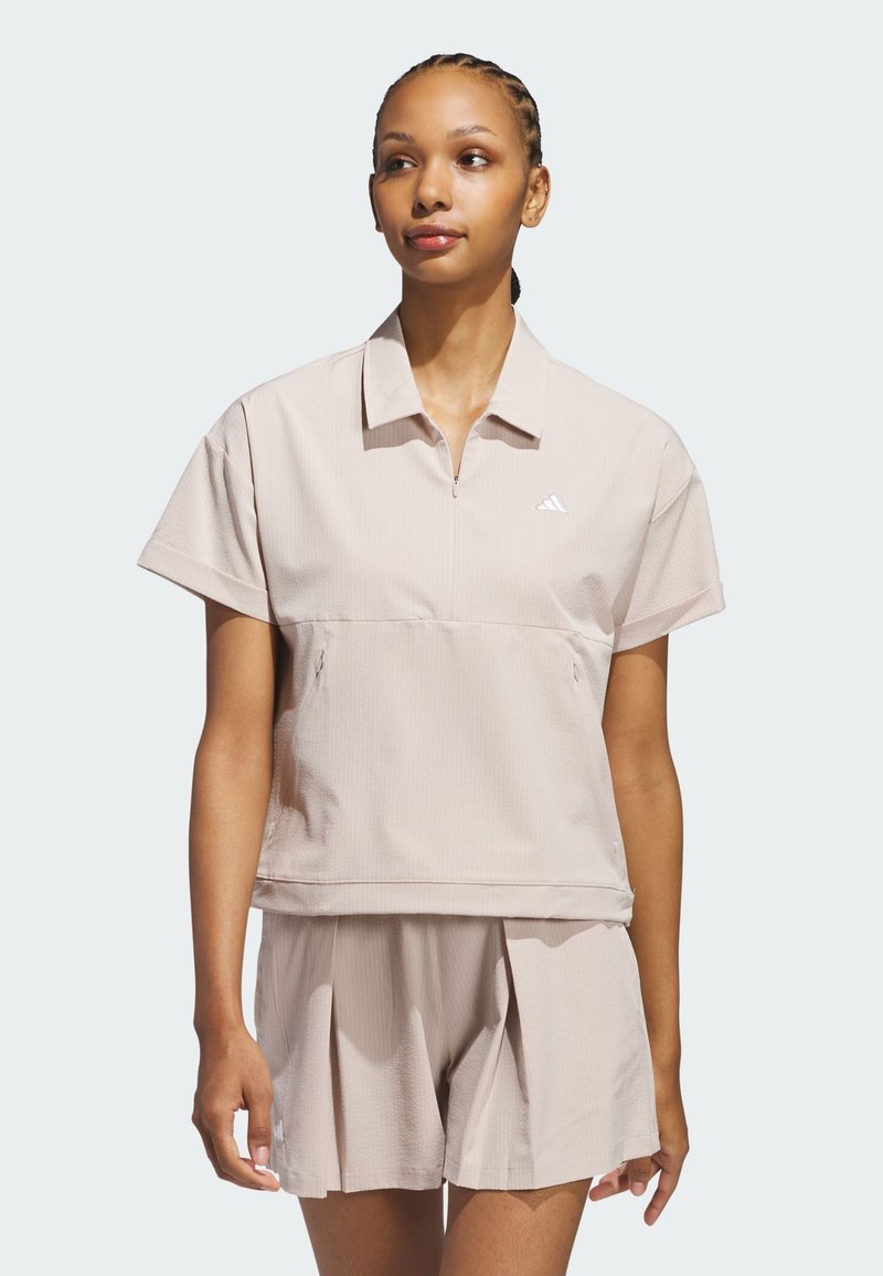 Ljusbeige träningsset bestående av en kortärmad zip-polo och veckade shorts, tillverkad av textil med strukturerad yta och embossad logodetalj.