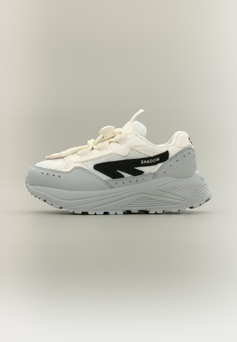 Fehér és szürke sportcipő vastag talppal, hálós felsőrésszel, fekete logócsíkkal "SHADOW" felirattal és húzózáras fűzővel, semleges háttéren bemutatva.