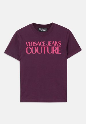 Violeta kokvilnas t-kreklu ar izteiksmīgiem rozā burtiem, kas krūtīs lasāmi "VERSACE JEANS COUTURE". Standarta apaļas apkakles dizains.