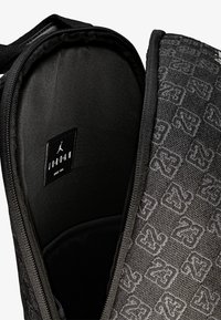 Musta seljakott, millel on tekstureeritud materjal ning õrn logomuster. Siseosa on sujuvast mustast kangast brändi etiketiga. Lukuga sulgemine.