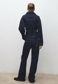 Tamno plavi traper jakna s pojasom u struku i širokim hlačama, s dvostrukim šavovima i ležernim dizajnom.