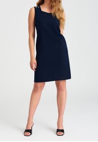Námorně modré bezrukávové šaty s kulatým výstřihem a stříbrnými knoflíky na rameni, se rovnými a pohodlnými liniemi.