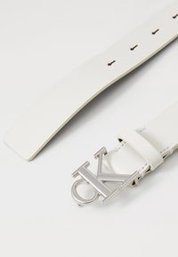 Fehér bőrövet ezüst hardware-rel és egy kiemelkedő "CK" logós csattal. Varrott részletek és több állítható lyuk található rajta.