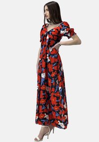 Abito lungo realizzato in tessuto leggero, caratterizzato da un vivace motivo floreale in rosso, blu e bianco, con maniche a sbuffo e un corpetto aderente.