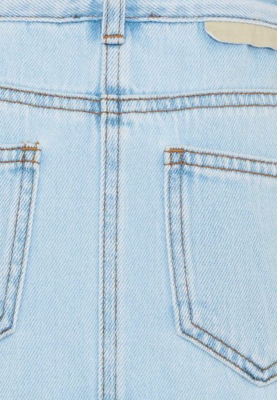 Gros plan sur l'arrière d'un jean en denim bleu clair avec deux poches et des coutures marron visibles le long des coutures et des bords des poches.