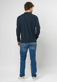 Mandens langærmede navy polo shirt, blanding af bomuld, rund krave, bæres med lyseblå denimjeans, der har en slim fit og synlig syning.