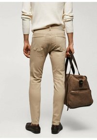 Pantalones beige de corte slim con bolsillos traseros, combinados con un bolso marrón, llevados con un suéter crema de canalé y zapatos oscuros. Diseño y textura sencillos.