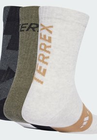 Tres pares de calcetines: gris oscuro con un patrón, verde oliva y blanco con una marca naranja; todos están tejidos con puños acanalados.