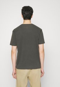 Camicia a maniche corte in cotone verde scuro, con scollatura a girocollo, dettagli cuciti e vestibilità morbida. Design semplice senza fantasie.