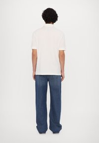 Hvid polo-shirt og løstsiddende blå jeans. Poloen har en klassisk krave og korte ærmer, mens jeansene har et lige ben-design.