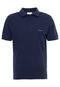 Mörkblå pikétröja i bomull med texturerad yta, treknappsknäppning och en liten svart Calvin Klein-logotyp på vänster bröst.