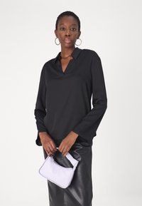 Top nero a maniche lunghe con colletto a V, abbinato a una gonna in pelle nera aderente. Tiene una piccola borsa color lilla chiaro con forma curva.
