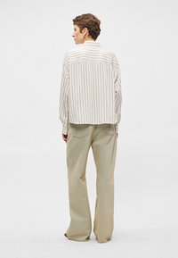 Svītrota viegla krekla ar brīvu piegriezumu, kombinēta ar mīkstiem zaļiem platām biksēm. Dabiski materiāli ar smalkām tekstūrām un neitrālām krāsām.