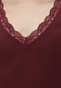 Vêtement bordeaux à col en V avec une délicate bordure en dentelle florale autour de l'encolure sur une peau claire.