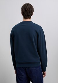 Sweat-shirt bleu marine en mélange de coton, avec un col rond et des poignets côtelés. La vue de dos montre une texture lisse et un design minimaliste.