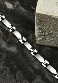 Bracciale in metallo argentato caratterizzato da segmenti rettangolari piatti e collegati. Ha una superficie liscia e lucida con finiture alternate lucide e opache.