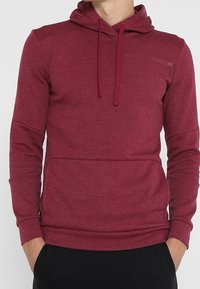 Sweat à capuche bordeaux en tissu doux avec poche kangourou, capuche à cordon de serrage et poignets côtelés. Texture lisse avec détails de coutures.