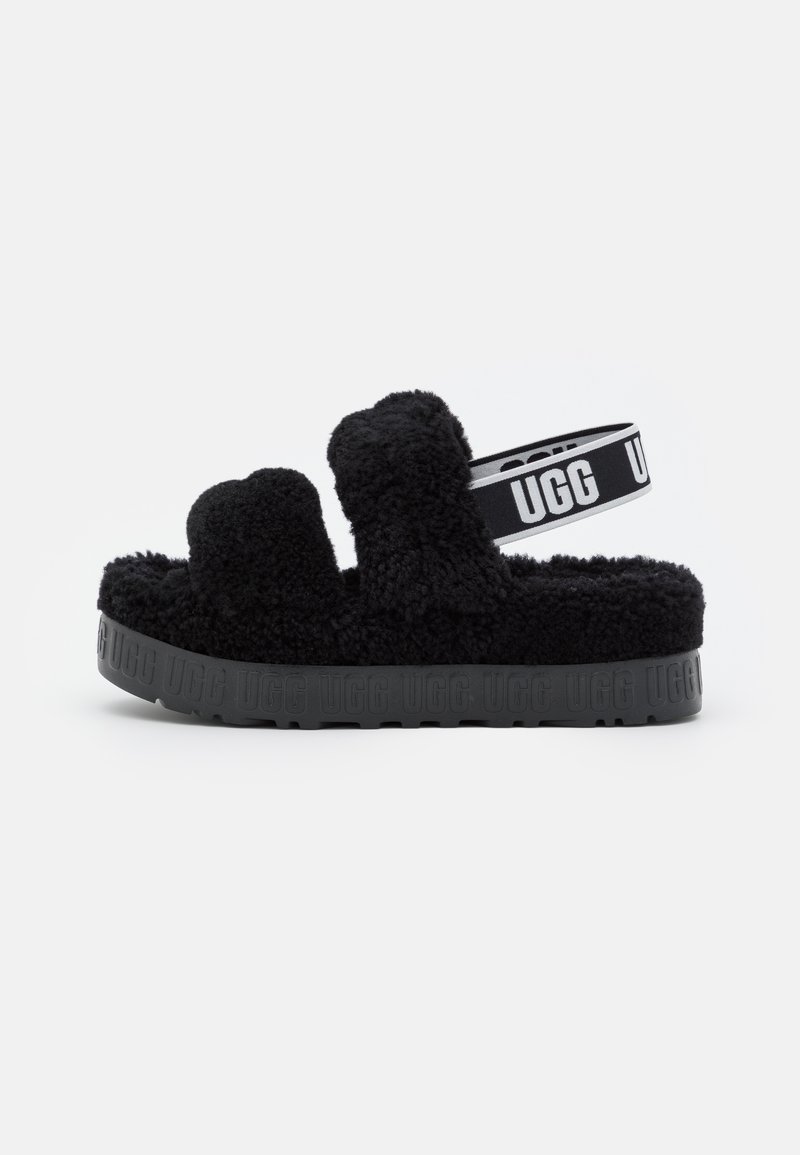 Sandalia de suelo negra y esponjosa con doble correa superior y suela de goma texturizada que presenta el logo de la marca en relieve en el lateral.