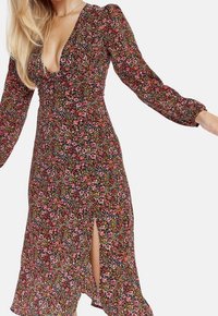 Blommönstrad klänning med djup V-ringning, långa puffärmar och slits fram. Materialet har en färgglad blandning av rosa, grönt och gult.