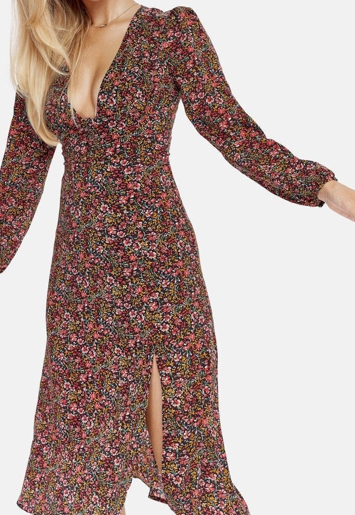 Blommönstrad klänning med djup V-ringning, långa puffärmar och slits fram. Materialet har en färgglad blandning av rosa, grönt och gult.