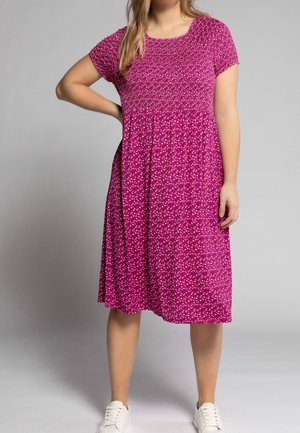 Korte mouwen jurk van felroze stof met witte en paarse polkadots, met een geplooide korset en een vloeiende rok. Gecombineerd met witte sneakers.