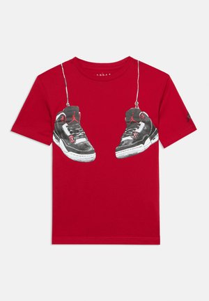 Red short-sleeve t-shirt with graphic of black and white Air Jordan sneakers hanging by their laces on the chest area.
