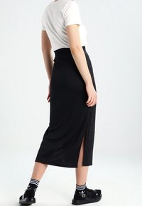 Svart midiklänning med hög midja och en sidolits, kombinerad med en vit kortärmad skjorta och svarta sandaler med mönstrade strumpor.