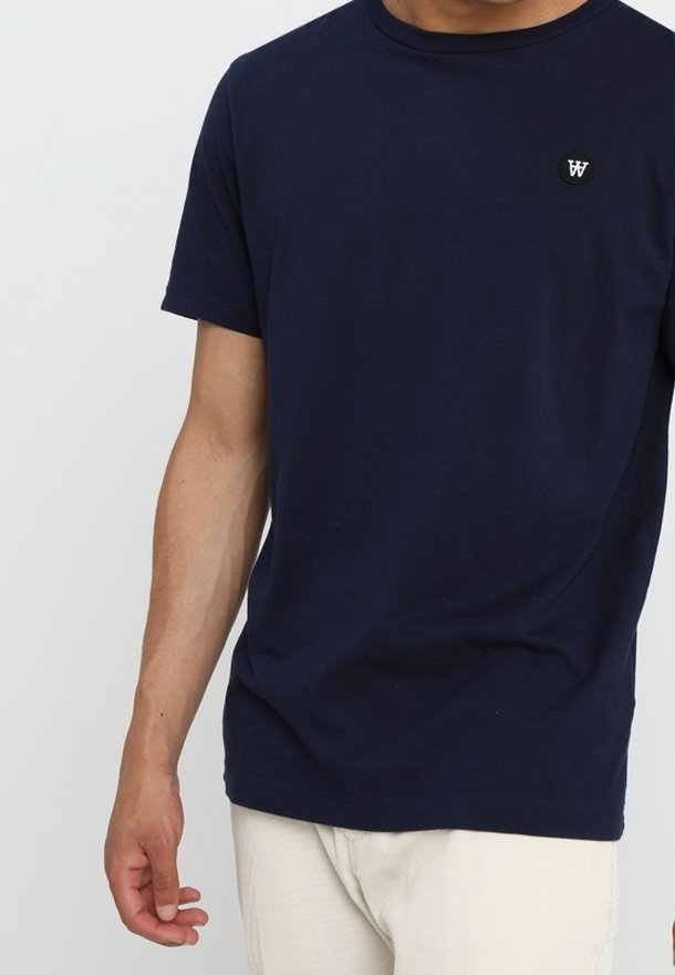 Námořnická modrá bavlněná tričko s kulatým výstřihem a krátkými rukávy. V horní levé části hrudníku má malé černé logo.