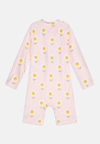 Lyserød langærmet jumpsuit med gule blomstermønstre, hvide kronblade, grønne stilke og en baggrund med prikker. Blødt, strækbart stof.