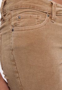 Bordeaux ribfluwelen broek met verticale ribbels, voorzien van een voorkantzak met stikdetails en zilverkleurige klinknagels op de tailleband.