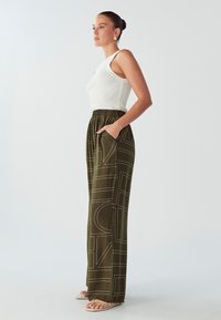 Maslinasto zelene hlače viskog struka, opuštenog kroja, s geometrijskim bijelim uzorkom i bočnim džepovima. Uparene s bijelim rebrastim majicom bez rukava.