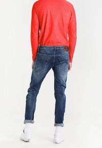 Tummansiniset farkut slim fit -mallissa, jotka on varustettu keskipitkällä vyötäröllä ja käärittyillä hihoilla. Takataskun ompeleet ovat näkyvissä, ja siinä on nahkaetiketti.