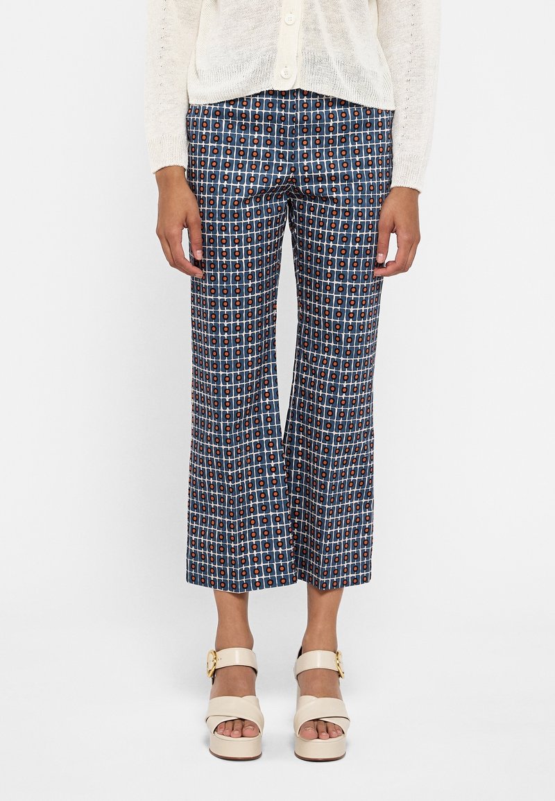 Jambes portant un pantalon court à motif bleu marine et blanc avec des points rouges, un haut en tricot crème boutonné, et des sandales compensées crème avec boucles.