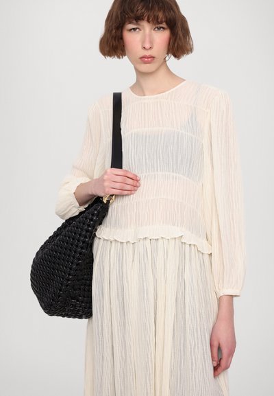 Black woven handbag with a curved shape and a textured surface, paired with a light cream, pleated blouse and skirt.