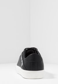 Mustat nahkakengät pyöreällä varvalla, valkoisella pohjalla ja teksturoidulla päällyksellä. Kengissä on kontrastivärinen logo sivussa ja pehmustettu nilkkareuna.