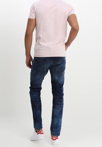 Vaqueros de un azul oscuro con un patrón desgastado, de corte ajustado, cinco bolsillos y cintura media, combinados con una camisa de manga corta rosa claro y zapatillas blancas.