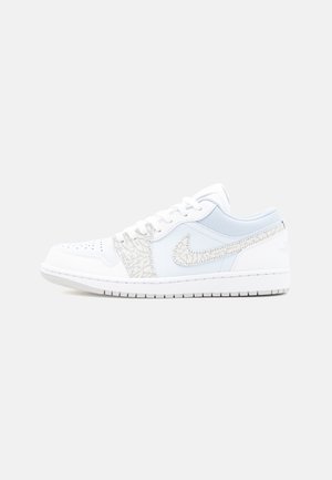 Zapatilla blanca de caña baja con logo Nike en gris claro texturizado y detalles en los cordones, puntera perforada y suela acolchada.