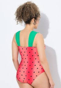 Punainen uimapuku yhdestä osasta, jossa on vesimelonin kuviota, mustia siemeniä ja vihreitä olkaimia. Pehmeä rakenne, istuva muotoilu ja kohtuullinen peittävyys.