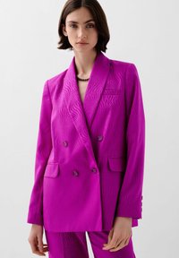 Blazer de doble botonadura en un vibrante fucsia con un sutil patrón de olas, solapas con muesca, dos bolsillos frontales y botones a juego.