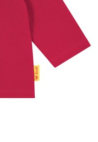 Red long-sleeve shirt sleeve with yellow Steiff brand tag attached near the hem.
