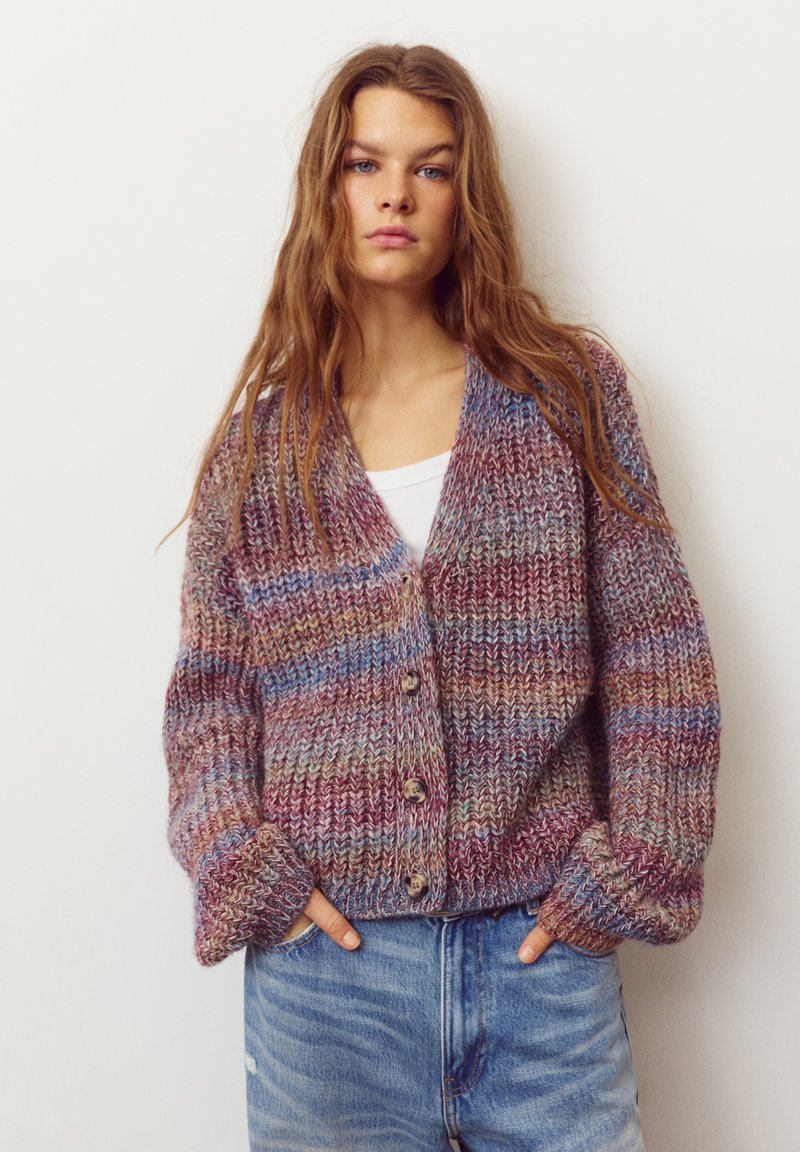 Cardigan tricotat colorat, cu croială largă, cu nasturi mari și o combinație de tonuri mov, albastre și pământii. Țesătură texturată, confortabilă.