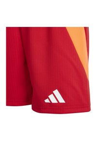 Rode sportshorts met een oranje diagonale streep en een wit Adidas-logo vlakbij de zoom aan de linkerpijpen.