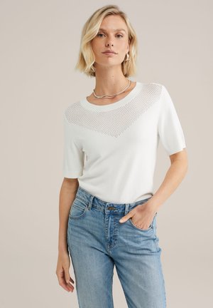 Tricou alb din tricot, cu mâneci scurte, având un design perforat la umeri și o croială lejeră, asortat cu blugi din denim de culoare bleu deschis.
