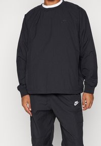 Black, long-sleeve Nike pullover with crew neck, elastic cuffs, and logo on the chest. Made of lightweight fabric with a smooth texture.