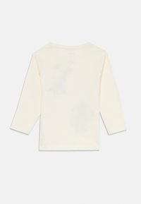 Camicia a maniche lunghe color crema, realizzata in tessuto morbido, presenta un semplice scollo rotondo e lati senza cuciture, con un leggero motivo di dinosauri sul retro.