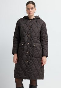 Bruine gewatteerde jas met een capuchon, voorzien van goudkleurige hardware, twee vo zakken en een langere pasvorm met ruitvormige stiksel.