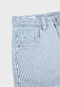 Blaue und weiße, vertikal gestreifte Jeans aus Denim mit Vordertasche, Gürtelschlaufen und Metallnieten vor weißem Hintergrund.