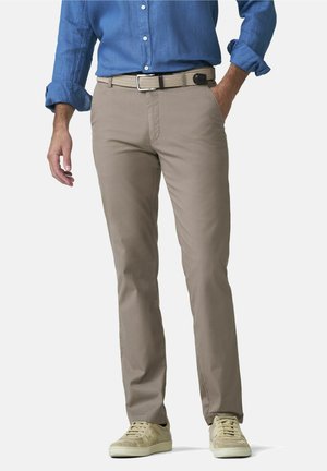 Homme portant un pantalon beige, une ceinture tissée beige, des baskets crème et une chemise bleu à manches longues boutonnée avec les manches retroussées.