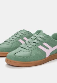 Chaussures de sport vertes avec des accents roses. Fabriquées à partir d'un mélange de matériaux synthétiques et de daim, avec une semelle en gomme texturée et un système de laçage.